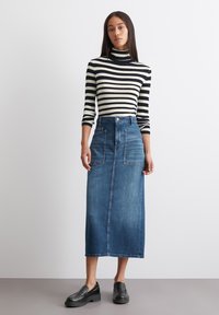 Maglietta a righe a maniche lunghe con colletto alto abbinata a una gonna di jeans di media lunghezza con due tasche frontali. Scarpe nere slip-on completano l'outfit.