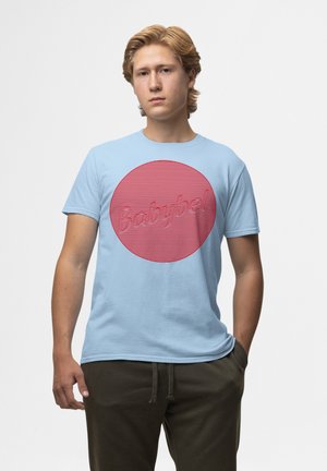 Helles blaues Baumwoll-T-Shirt mit einem großen roten, kreisförmigen Grafikdesign, das das Wort "Babybel" in erhabener Schrift zeigt. Kurze Ärmel und Rundhalsausschnitt.