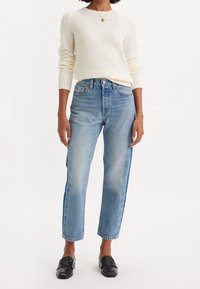 Suéter de punto crema con puños acanalados, jeans de pierna recta de talle alto en azul claro y mocasines negros. Diseño minimalista con corte clásico.