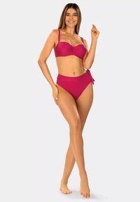 Fuksjowy zestaw bikini z teksturowanym topem bandeau i wysokim stanem dołu z detalem w postaci wiązania z boku. Gładki materiał i minimalistyczny design.