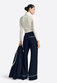 Krém színű garbó pulóver tengerészkék, széles szárú nadrággal, mely fehér részleteket tartalmaz, kezében pedig hozzáillő dzseki. Sima, puha textúrák.