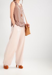 Top senza maniche in bronzo con motivo e fiocco, pantaloni larghi crema, scarpe con zeppa arancioni e borsa color tan. Texture morbide e colori delicati.