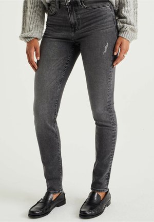 Jeans skinny grises con una cintura alta y un ligero desgaste. Combinándolos con mocasines negros, que muestran una textura suave y un ajuste clásico.