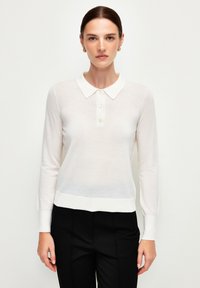 Witte langwerpige polo trui met een kraag, knoopsluiting en geribde manchetten. Lichtgewicht, iets doorzichtig materiaal met een aansluitende pasvorm.