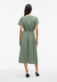 Vestido verde de longitud media con mangas cortas y cinturilla elástica. Hecho de una tela suave, presenta un diseño simple y fluido.