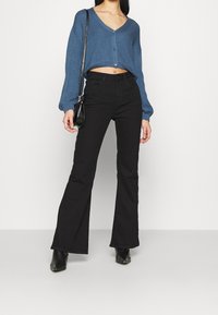 Een kort, geribbeld, blauwe trui met een V-hals en knoopsluiting, gecombineerd met hooggewende, zwarte flared jeans en zwarte enkellaarsjes.