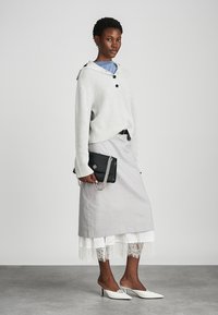 Light gray ribbed sweater with a hood and buttons, paired with a gray skirt layered over white lace. Black clutch bag and white mules.