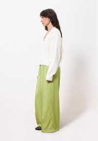 Weißer Strickpullover mit V-Ausschnitt und langen Ärmeln, kombiniert mit weit geschnittenen, hellgrünen Hosen. Strukturiertes Muster auf dem Pullover und klare Linien.