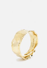 Gold band ring with a wavy design, featuring a polished surface and subtle textural detail. Inscription visible on the inner band.