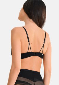Soutien-gorge noir avec bretelles ajustables et un fermoir à crochets. Tissu lisse avec un design minimaliste et un détail matériel subtil.