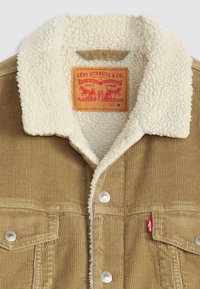 Veste en velours côtelé marron avec un col en fausse fourrure blanche. Dotée de boutons-pression en métal et d'une étiquette rouge Levi's à l'avant. Taille M.