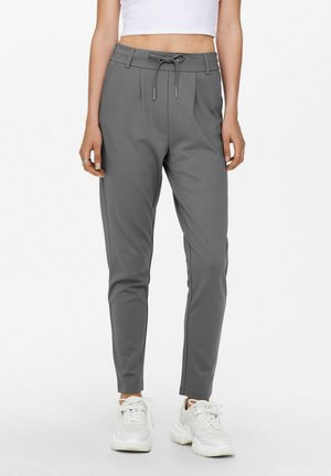 Šedé jogger kalhoty s elastickým pasem a bočními kapsami, se smooth texturou a slim fit designem, doplněné o bílé sportovní boty.