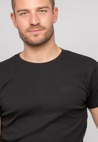 T-shirt noir en coton à col rond avec des manches courtes et un logo discret sur la poitrine, texture lisse et coupe classique.