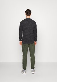 Slim-fit, texturovaný tmavě šedý svetr s kulatým výstřihem, doplněný olivově zelenými kalhotami a šedými teniskami. Viditelné rukávy a zadní část.