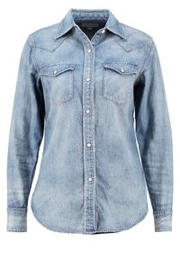 Ljusblå denimskjorta med lång ärm, spetsig krage, två bröstfickor och tryckknappsstängning. Har en böjd nederkant och en urblekt textur.