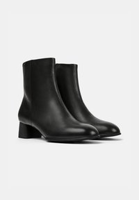 Botas de tobillo de cuero negro con una textura suave, punta redonda y tacón cuadrado. Presentan un diseño limpio y minimalista sin herrajes visibles.