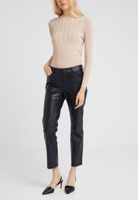 Top à manches longues beige avec une silhouette ajustée, associé à un pantalon en cuir noir slim et des escarpins noirs à talons pointus.
