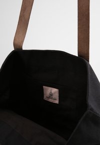 Sac fourre-tout en toile noire avec une bandoulière en daim marron et une poche intérieure. Présente une étiquette en tissu avec le logo "Beck Søndergaard".