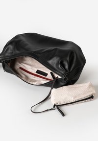 Zwarte leren tas met een gestructureerde oppervlakte, voorzien van een ritsafsluiting, rode binnenzak en een kleine met een patroon versierde tas, ook met rits.