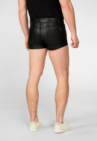 Zwarte leren shorts met een slim fit, voorzien van twee achterzakken en contrasterende stiksels. Gstyled met een eenvoudig zwart t-shirt en lichte sneakers.