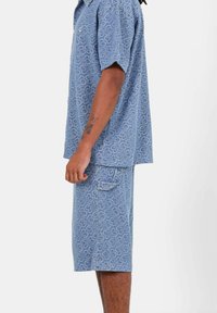 Conjunto de camisa de manga corta y pantalones cortos en azul claro con un patrón abstracto en toda la superficie. La tela parece texturizada y suave; cuenta con un bolsillo.