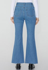 Vaqueros acampanados de color azul desvaído con cintura alta, dos bolsillos traseros y detalles de costura mínimos. El tejido parece suave y ligero.