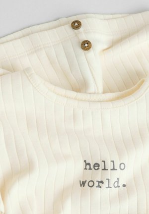 Béžový žebrovaný dětský overal má kulatý výstřih, dva dřevěné knoflíky a potisk s textem "hello world."