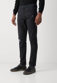 Crne traperice od denima slim fit kroja s iznošenim detaljima. Imaju klasične džepove i zatvaranje na gumb. Upareno s crnim tenisicama.