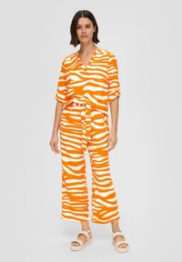 Orange und weiße Zebra-Streifen passende Kombination bestehend aus einem locker sitzenden Kurzarmoberteil und weiten Hosen, gefertigt aus leichtem Stoff.