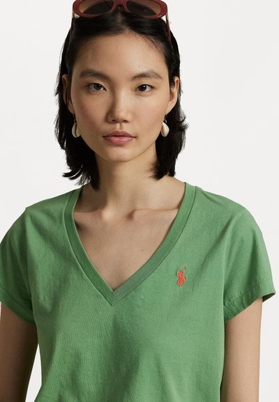 Green cotton t-shirt with a V-neck design, featuring short sleeves and a red embroidered logo on the chest. Smooth texture.
