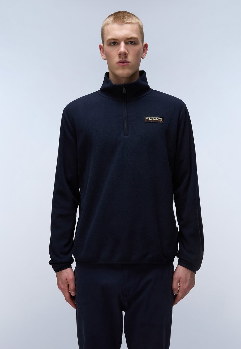 Pullover de forro polar ligero en azul marino con media cremallera, que presenta un pequeño parche de logo en el pecho. Textura suave y mangas largas.