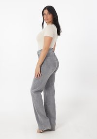 Camiseta ajustada de un beige claro combinada con unos jeans de talle alto de campana en gris claro. Tejido suave con detalles de costura mínimos y sin patrones.