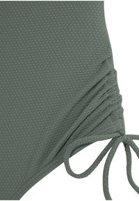 Maillot de bain vert texturé avec un motif en nid d'abeille. Comprend des détails froncés sur les côtés et des liens ajustables pour un maintien sécurisé.