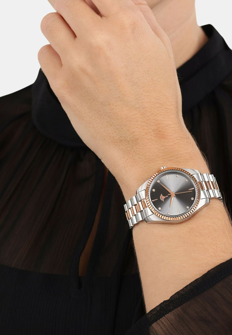 Silberne und roségoldene Armbanduhr mit einem runden grauen Ziffernblatt, silbernem Metallarmband und funkelnden Stundenmarkierungen, getragen an einer Hand vor einem dunklen Stoff.