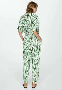 Groen en witte gestreepte jumpsuit met een losse pasvorm, korte mouwen, tailleband en zakken. Gemaakt van een lichte stof.