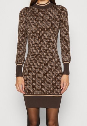 Femme portant une robe en maille marron ajustée avec un motif losange beige et des manches longues, debout les bras relâchés le long du corps.