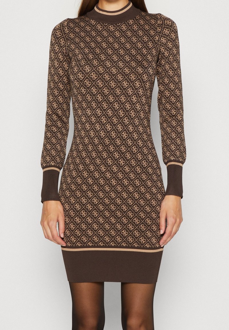 Femme portant une robe en maille marron ajustée avec un motif losange beige et des manches longues, debout les bras relâchés le long du corps.