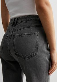 Vysoké šedé džíny vyrobené z džínoviny, které mají klasický pětipocketový design a jemné švy. Měkká textura a přiléhavý silueta.