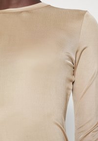 Langärmliges Oberteil in einem hellbeigen, glatten, dehnbaren Stoff mit tailliertem Design und rundem Ausschnitt; minimale Nähte und dezenten Glanz.