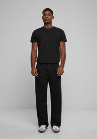 Camiseta negra de manga corta con cuello redondo, combinada con pantalones holgados negros y zapatillas blancas con detalles en gris.