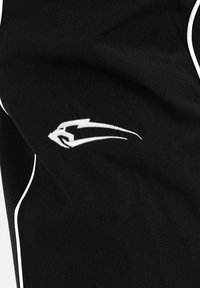 Tissu noir avec passepoil blanc et logo abstrait de tête d’aigle brodé en blanc sur la zone poitrine d’un vêtement.