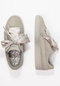 Zapatillas de gamuza gris claro, con cordones de satén anchos, suela texturizada y plantilla con un patrón que incluye un logo.