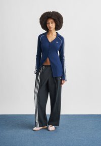 Navy ribbed button-up top with white accents, paired with black wide-leg pants featuring white side stripes and light pink ballet flats.