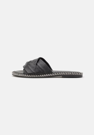 Black leather slide sandal with knotted upper, flat sole, and white stitched edging. Minimalist design with soft texture.