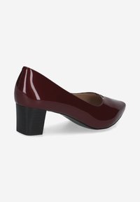 Escarpin en cuir verni bordeaux avec un bout pointu et un talon carré. La chaussure présente une finition lisse et un subtil détail découpé sur le bout.