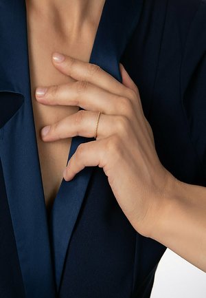Goldener Ring mit verdrehter Textur, getragen an einer Hand, die natürliche Hauttöne zeigt. Der Hintergrund zeigt ein dunkelblaues Kleidungsstück.