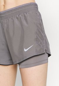 Pantalones cortos para mujer de Nike en gris claro, con un material ligero y suave, paneles laterales perforados y un detalle de logo blanco.