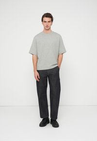 Γκρι κοντομάνικη μπλούζα σε συνδυασμό με χαλαρής γραμμής σκουρόχρωμο τζιν παντελόνι και μαύρα παπούτσια. Απλός σχεδιασμός με καθαρή σιλουέτα και ελάχιστες λεπτομέρειες.