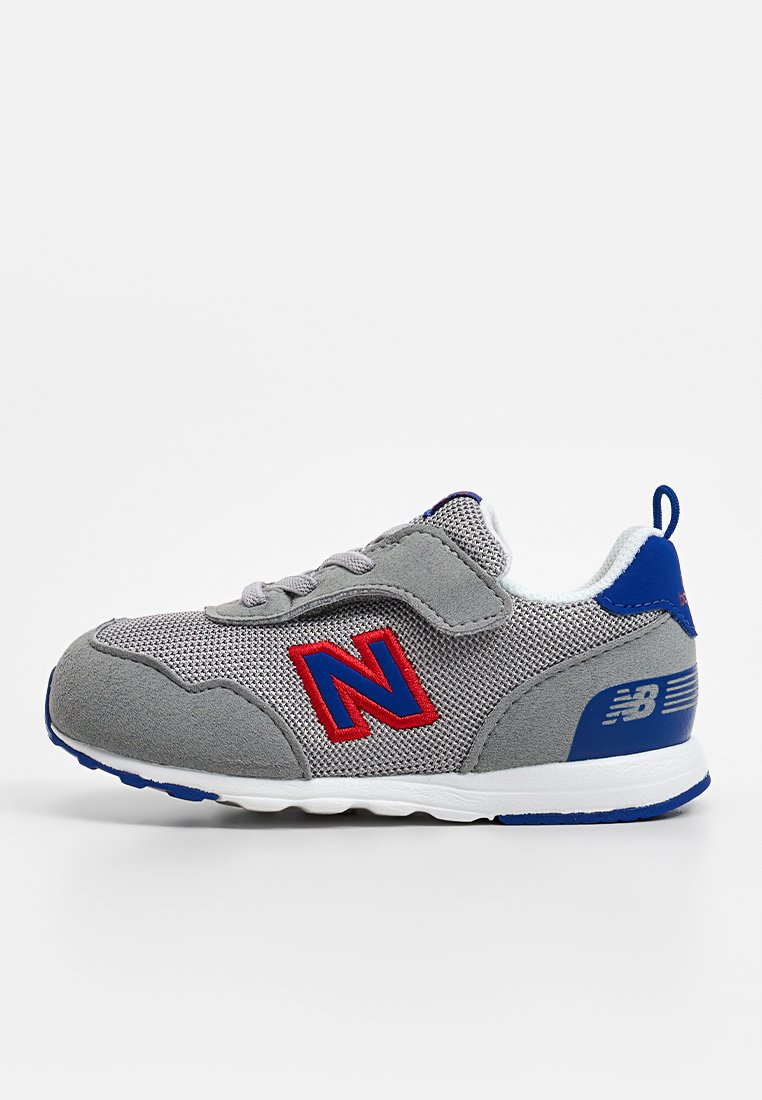 Scarpa da ginnastica grigia realizzata in materiali mesh e suede, con dettagli rossi e blu, lacci e una suola bianca. Logo distintivo sul lato.