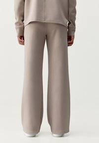 Kalhoty s širokými nohavicemi z měkkého taupe materiálu, které mají hladký povrch, elastický pas a manžety na kotnících.